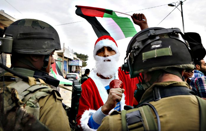 Palestinian protester dressed as Santa Claus holds a Palestinian